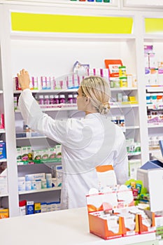 Junior pharmacist taking medicine from shelf