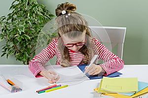 A junior schoolgirl with glasses writes something with her left