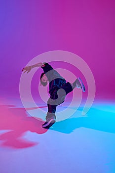 Junior street dancer in dynamic pose dressed in all black in mixed neon light against vibrant gradient background.