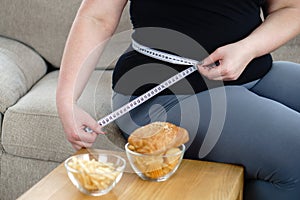 Junk eating. overweight woman measures waist girth