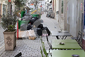 junk overflowing garbage containers on Paris sidewalk next to cafe