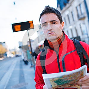 Just arrived: handsome young man studying a map on a bus stop