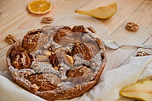 Just backed powdered pear pie decorated with white cloth, dried orange, walnuts, anise stars and spoon on the wooden board