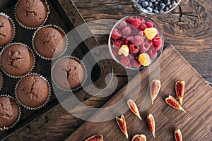 Just baked chocolate cupcakes in bakeware and seasonal fruits and berries. Flat lay. Top view