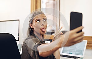 Just a bit of selfie silliness. a young businesswoman sticking out her tongue while taking selfies in an office.