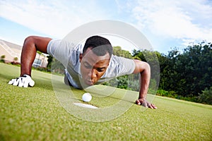 Just a centimeter away from success. a handsome man trying to blow his golf ball into the hole.