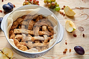 Just cooked homemade american apple pie in baked form on brown wooden table with raisins and fresh fruits - apples, grapes, plums