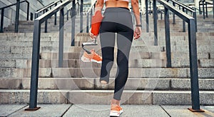 Just do it. Back view of disabled women in sports clothing holding her leg prosthesis while standing on stairs outdoors