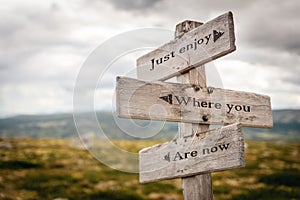 just enjoy where you are now text engraved on old wooden signpost outdoors in nature