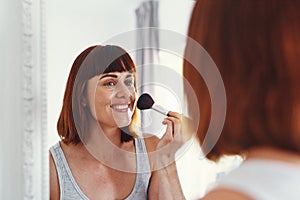 Just getting my glow on. an attractive young woman applying makeup on her face inside her bathroom at home.