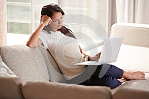 Just having a peaceful day at home. an attractive young woman sitting on the couch with her laptop.