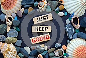 Just keep going symbol. Wooden blocks with words `Just keep going`. Beautiful black background, seashells and sea stones. Busine