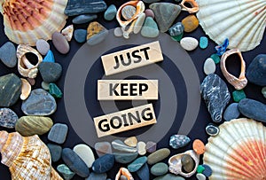 Just keep going symbol. Wooden blocks with words `Just keep going`. Beautiful black background, seashells and sea stones. Busine