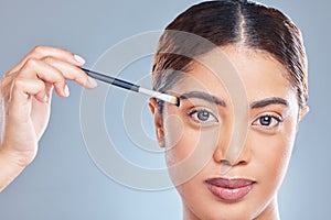 Just a little bit on here. a young woman applying makeup to her face against a grey background.