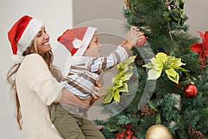 Just a little helping hand. Shot of a young boy decorating a christmas tree with his mothers help.