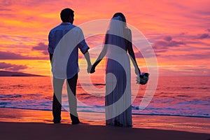 Just married couple holding hands on the beach at sunset