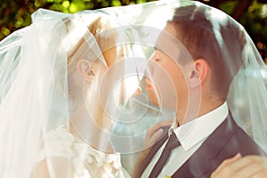 Just married couple kiss standing under a veil in the shine of m