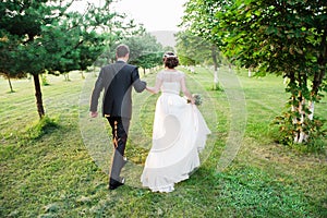 Just married couple running away in a green summer garden