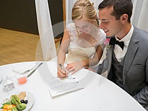 Just-married couple signing a prenup paper on a white table under the lights