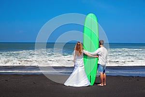 Just married couple stands with surfboard on sea beach