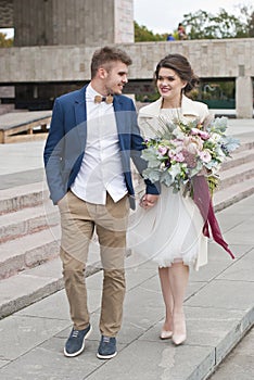Just married loving couple in wedding dress and suit . Happy bride and groom walking running in the summer city.