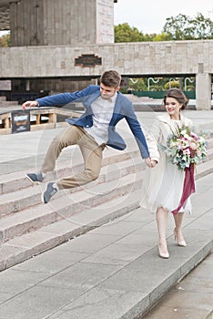 Just married loving couple in wedding dress and suit . Happy bride and groom walking running in the summer city.