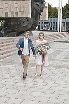 Just married loving couple in wedding dress and suit . Happy bride and groom walking running in the summer city.