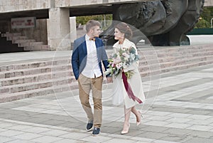 Just married loving couple in wedding dress and suit . Happy bride and groom walking running in the summer city.