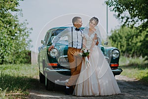 Just married wedding couple is standing near the retro vintage car in the park. Summer sunny day in forest. bride in