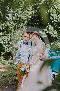 Just married wedding couple is standing near the retro vintage car in the park. Summer sunny day in forest. bride in