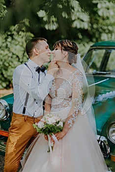 Just married wedding couple is standing near the retro vintage car in the park. Summer sunny day in forest. bride in