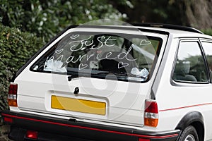 Just married written on back of classic white wedding day car with love heart back window.