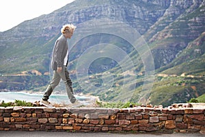 Just me and Mother Nature. a young man walking on a stone wall with the mountain in the background.