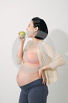 Just one apple a day. Beautiful young pregnant woman with smile and holding green apple while standing at white background