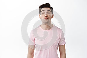 Just one kiss. Cute man pucker lips and waiting for kissing, looking hopeful at camera, standing against white