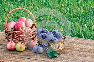 Just picked plums and apples in wicker baskets on old wooden boards