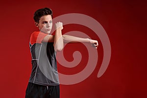 Just start. A teenage boy is engaged in fitness, he is looking aside while doing exercise. Isolated on red background