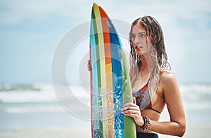 Just the surf and her board today. an attractive young woman standing on a beach with a surfboard.