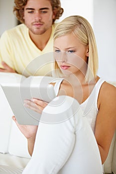 Just taking a peek. A beautiful young woman using a tablet as her boyfriend watches from over her shoulder.
