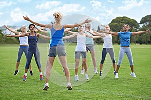Just ten more. A group of young women doing jumping jacks on a sportsfield.