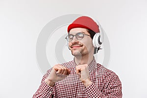 Just vibing. Happy carefree young hipster guy with moustache in glasses and red beanie dancing joyfully, listening to