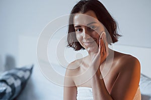 Just waking up. Time for a make up. Woman sits on the bed and use cosmetics to clean her skin