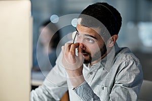 Just when you thought you could clock out. Shot of a young man feeling stressed while using a headset and computer late