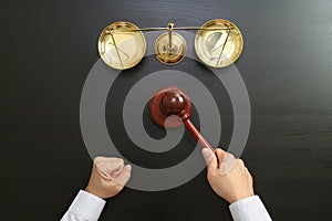 justice and law concept.Top view of Male judge hand in a courtroom with the gavel and brass scale on dark wood table