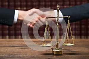 Justice Scale On Table With Judge And Client Shaking Hands