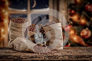 Jute sack with fresh coffee beans on wooden board with christmas decorations background. Christmas tree with ornaments and lights.