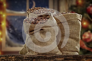 Jute sack with fresh coffee beans on wooden board with christmas decorations background. Christmas tree with ornaments and lights.