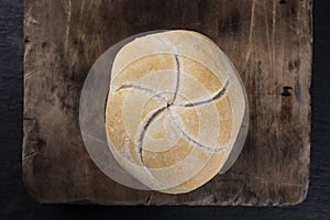 The Kaiser bread roll. A crusty round bread roll on a wooden cutting board
