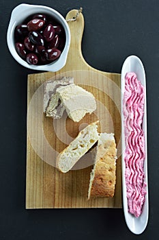 Kalamon olives on bowl, sunflower halva and lagana bread on cutting board and olive dish with taramosalata