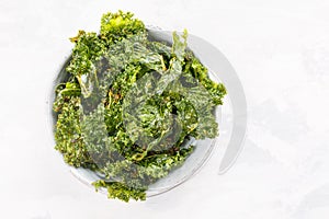 Kale chips in bowl. Crispy green kale chips dehydrated with salt, oil and vegan cheese. Healthy homemade vegan snack